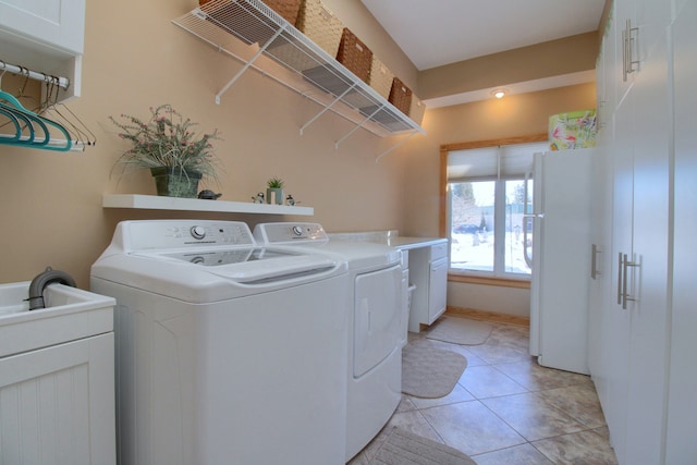 clothes washing area with cabinet space, light tile patterned floors, and washing machine and clothes dryer