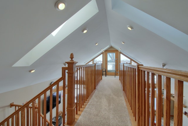 hallway with lofted ceiling with skylight and light colored carpet