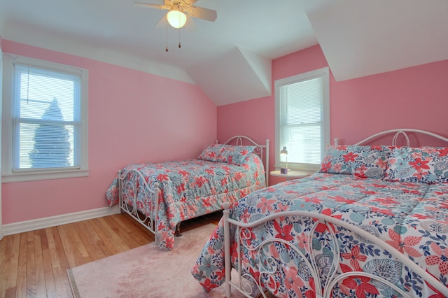 bedroom featuring lofted ceiling, multiple windows, baseboards, and wood finished floors