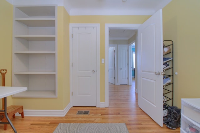 hallway with light wood-style floors, visible vents, built in shelves, and baseboards