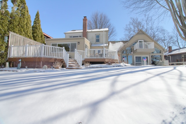 snow covered house featuring a deck and a chimney