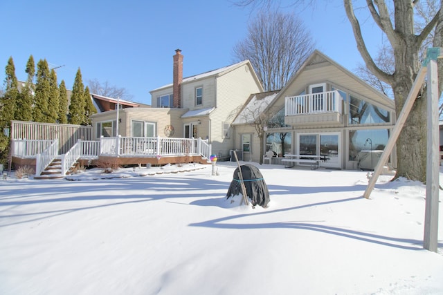 snow covered back of property featuring a balcony, a chimney, and a wooden deck