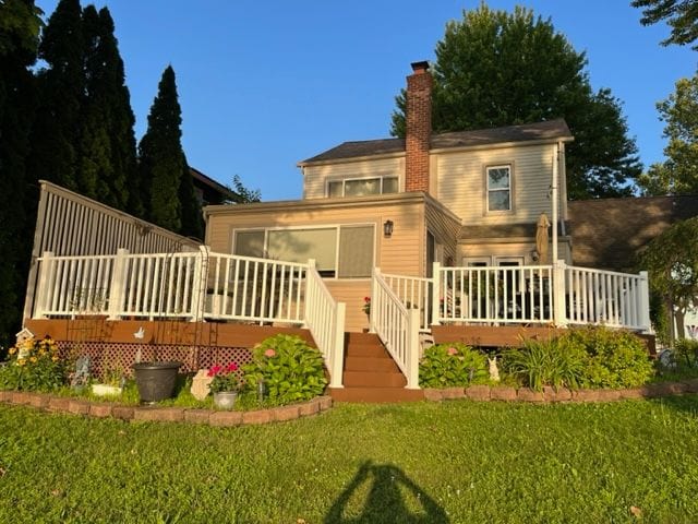 view of front of house with a chimney, a deck, and a front lawn