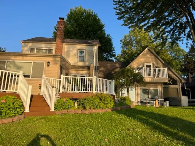 rear view of house featuring a chimney, a lawn, and a wooden deck