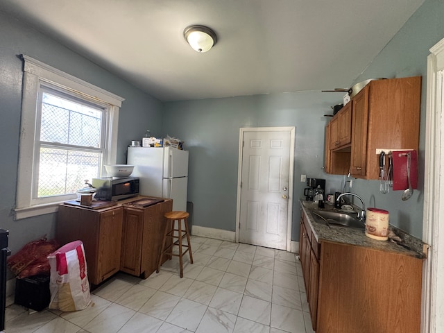 kitchen with dark countertops, a sink, brown cabinetry, marble finish floor, and stainless steel microwave