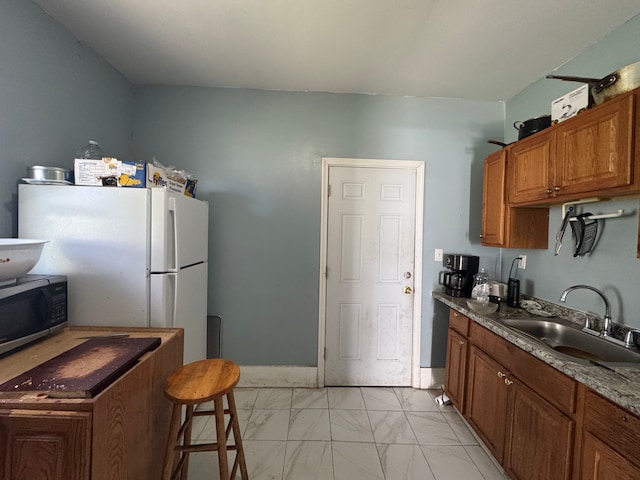kitchen featuring brown cabinets, a sink, stainless steel microwave, freestanding refrigerator, and marble finish floor
