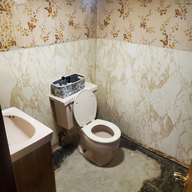 half bathroom with vanity, toilet, and wallpapered walls