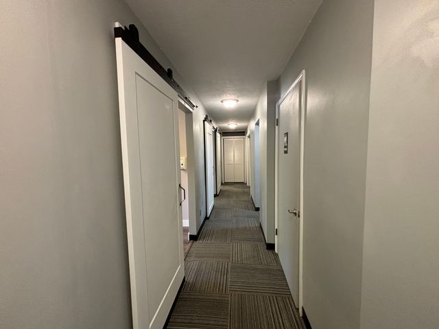 corridor with dark colored carpet, baseboards, and a barn door