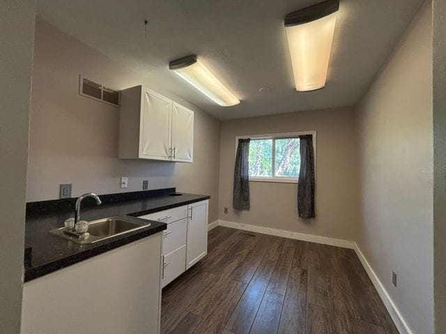 kitchen featuring dark wood finished floors, dark countertops, visible vents, white cabinets, and a sink