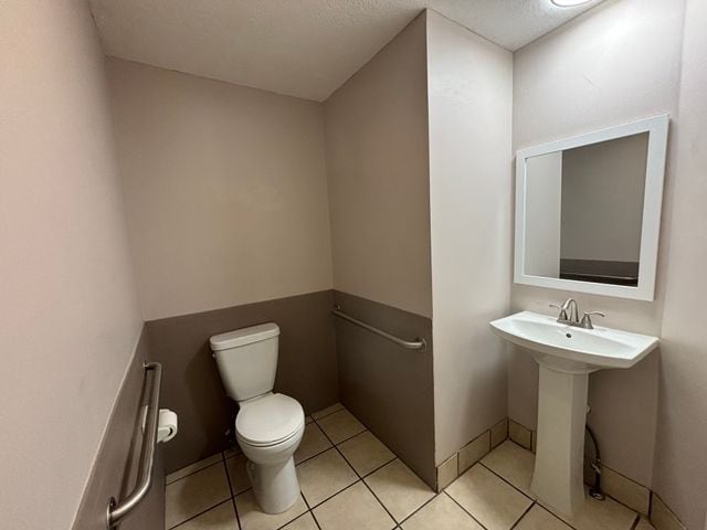 half bath with tile patterned flooring, baseboards, a sink, and toilet