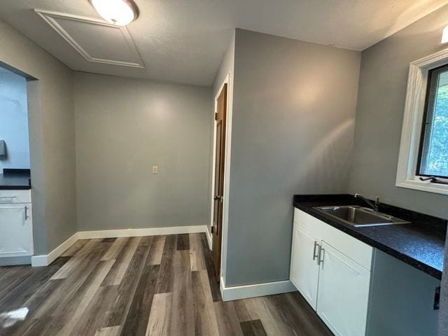 kitchen featuring baseboards, white cabinets, dark countertops, dark wood-style flooring, and a sink