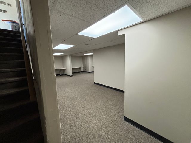 finished below grade area featuring light carpet, stairway, a drop ceiling, and baseboards