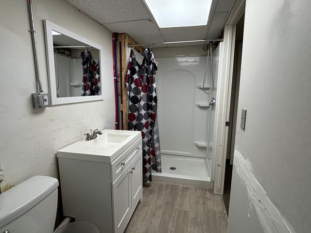 full bathroom featuring a drop ceiling, toilet, wood finished floors, vanity, and a shower stall