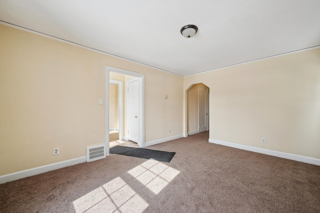 carpeted empty room with baseboards, visible vents, and arched walkways