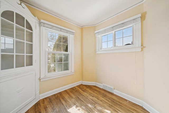 empty room featuring plenty of natural light, baseboards, visible vents, and wood finished floors