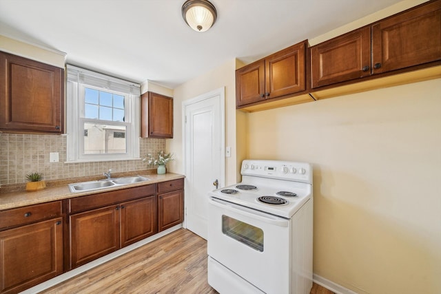 kitchen with light wood finished floors, tasteful backsplash, light countertops, white electric range, and a sink