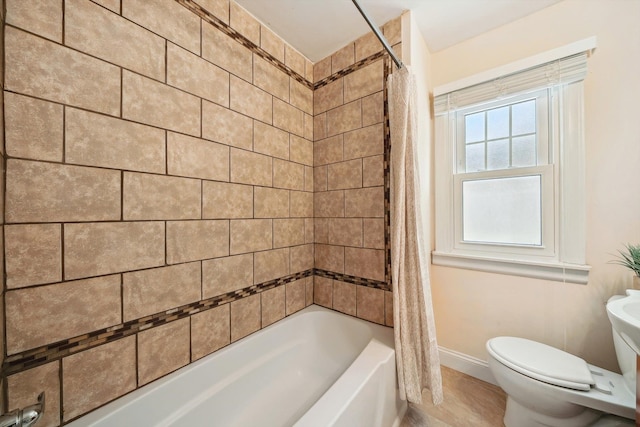 bathroom featuring toilet, shower / tub combo, and baseboards