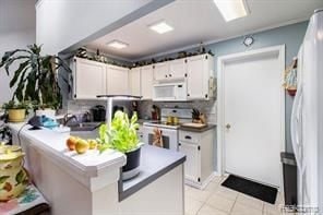 kitchen featuring light tile patterned floors, decorative backsplash, white cabinetry, a sink, and white appliances