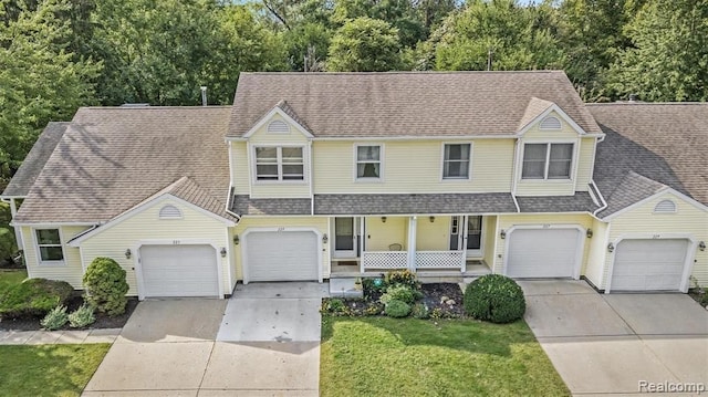 traditional home with a porch, concrete driveway, a shingled roof, and a front lawn