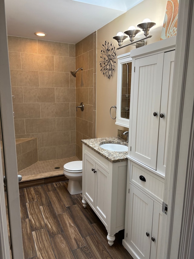 full bath featuring tiled shower, vanity, toilet, and wood finished floors