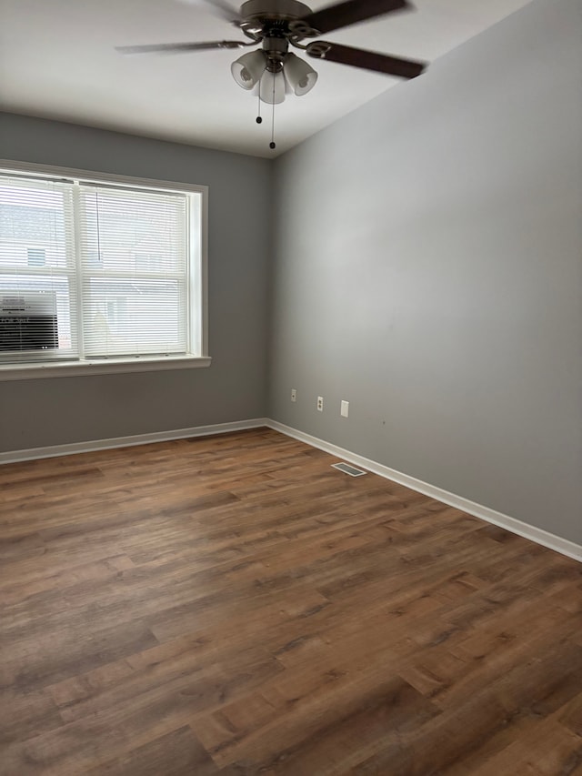 unfurnished room featuring dark wood-type flooring, a ceiling fan, visible vents, and baseboards