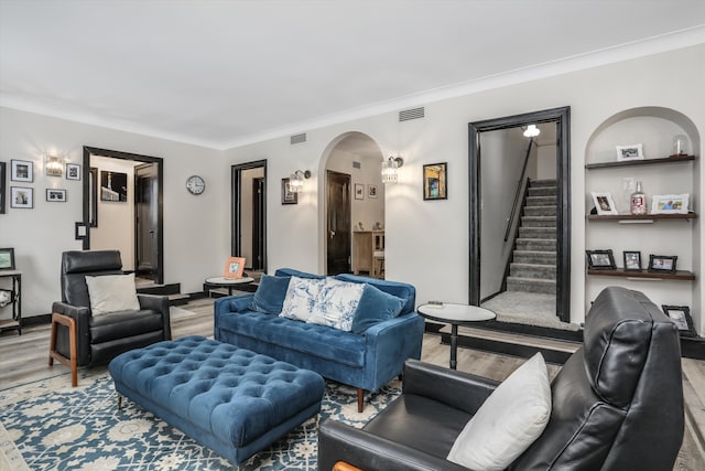 living area featuring arched walkways, crown molding, visible vents, stairway, and wood finished floors