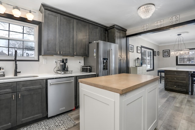 kitchen with a kitchen island, a sink, white cabinets, appliances with stainless steel finishes, and light wood finished floors