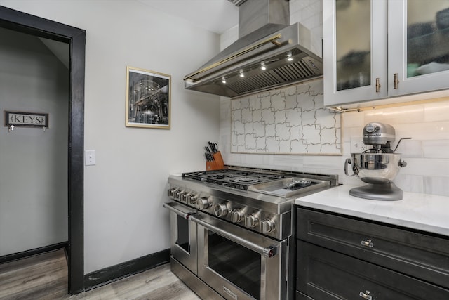 kitchen featuring range with two ovens, light countertops, range hood, decorative backsplash, and glass insert cabinets