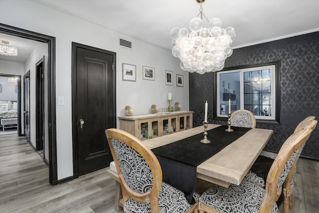 dining room featuring wallpapered walls, visible vents, light wood-style flooring, crown molding, and a notable chandelier