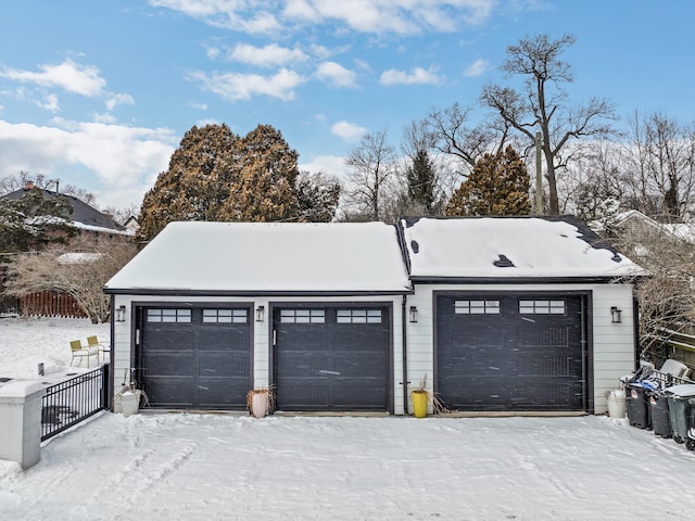 snow covered garage featuring a garage and fence