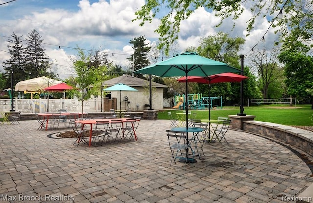 view of property's community with a lawn, fence, outdoor dining area, playground community, and a patio area