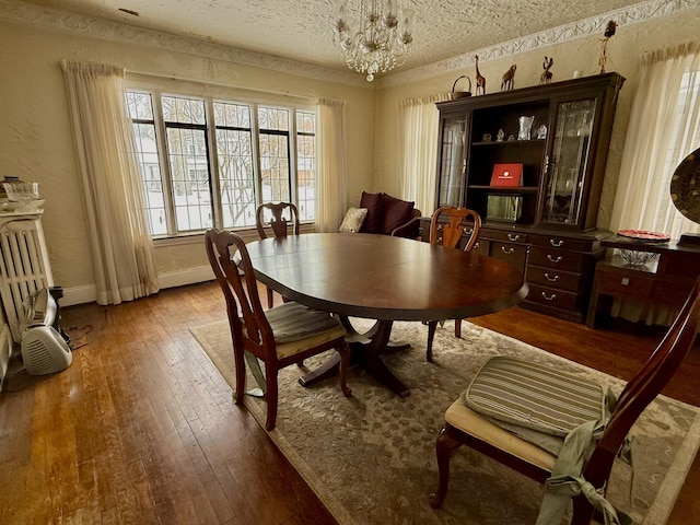 dining space with a notable chandelier, a textured ceiling, baseboards, and wood finished floors