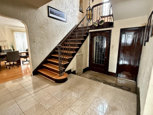 entryway featuring stairway, granite finish floor, arched walkways, and a textured wall