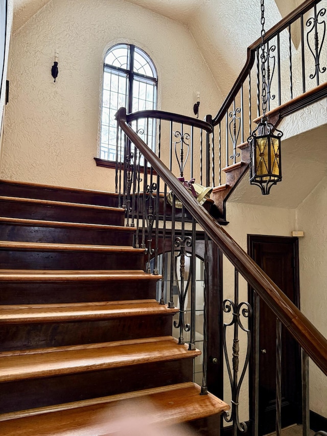 stairway featuring lofted ceiling and a textured wall