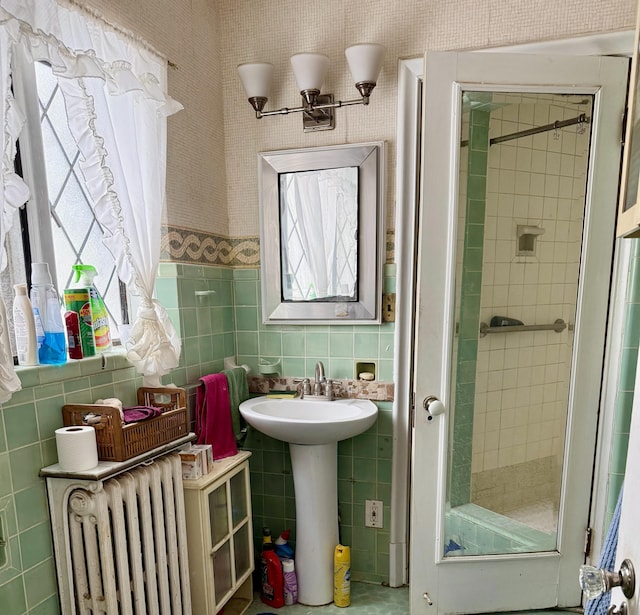 bathroom with tiled shower, radiator heating unit, a sink, and tile walls