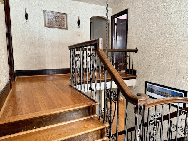 stairway featuring baseboards, arched walkways, wood finished floors, and a textured wall