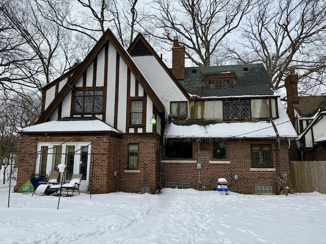 snow covered property featuring brick siding, a chimney, and stucco siding