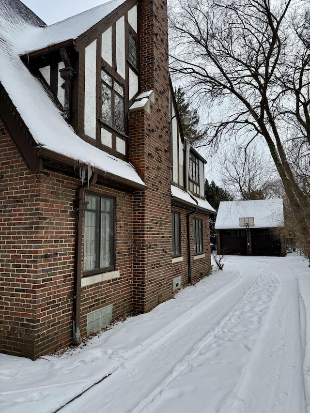 view of snowy exterior featuring brick siding and a chimney