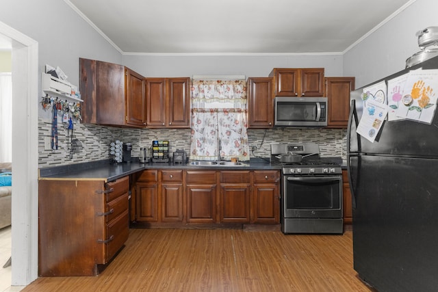 kitchen featuring stainless steel appliances, dark countertops, light wood-type flooring, and a sink