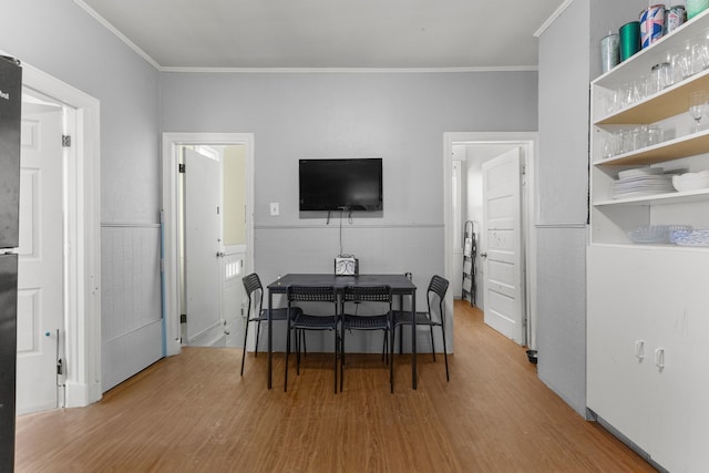 dining space with tile walls, ornamental molding, wood finished floors, and wainscoting