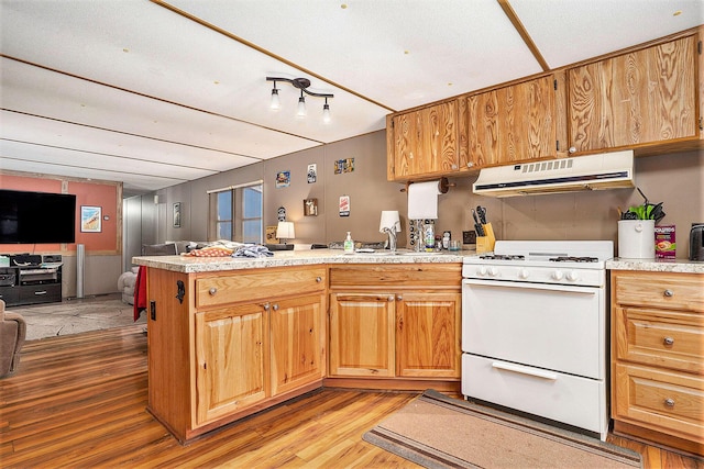 kitchen with light countertops, a peninsula, under cabinet range hood, and white range with gas cooktop