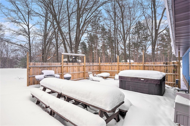 snow covered patio featuring a fenced backyard and a hot tub