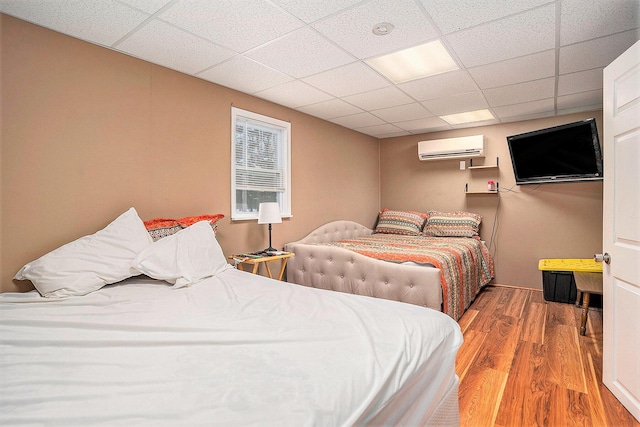 bedroom featuring a wall unit AC, a drop ceiling, and wood finished floors