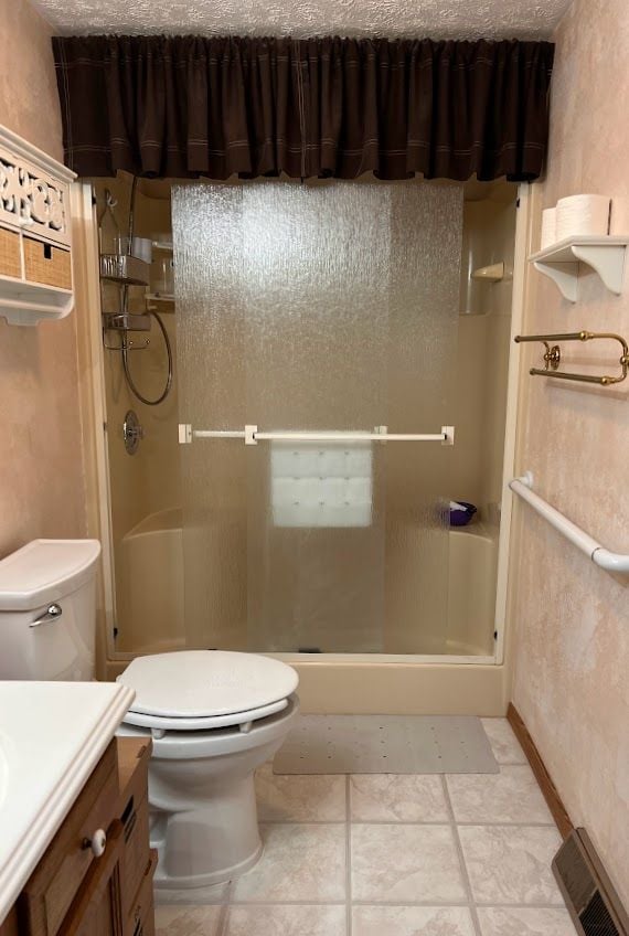 full bath featuring visible vents, toilet, vanity, a shower stall, and a textured ceiling