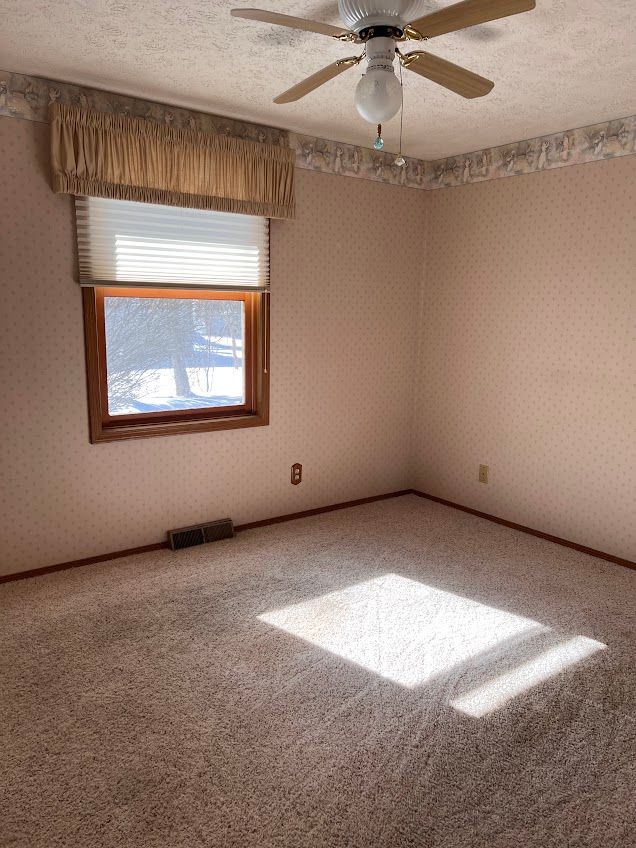 carpeted empty room with a textured ceiling, a ceiling fan, baseboards, visible vents, and wallpapered walls