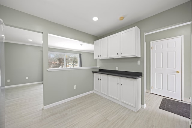 kitchen with dark countertops, white cabinetry, light wood finished floors, and baseboards