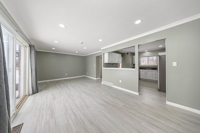 unfurnished living room featuring ornamental molding, light wood finished floors, visible vents, and baseboards