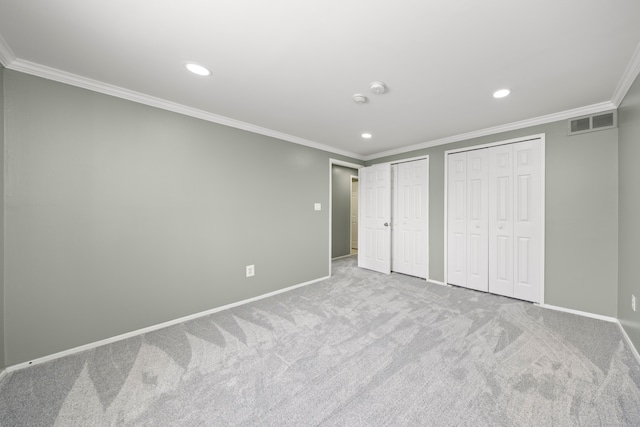 unfurnished bedroom with crown molding, multiple closets, visible vents, light carpet, and baseboards