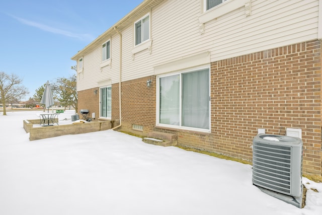 snow covered back of property featuring a patio, central AC unit, and brick siding