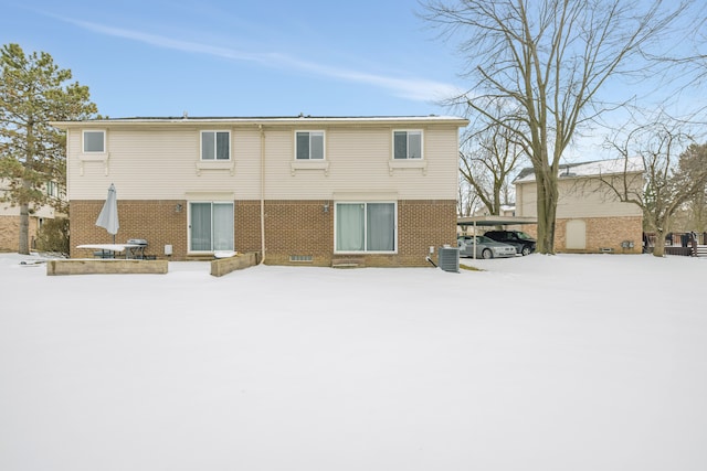 snow covered back of property featuring cooling unit and brick siding